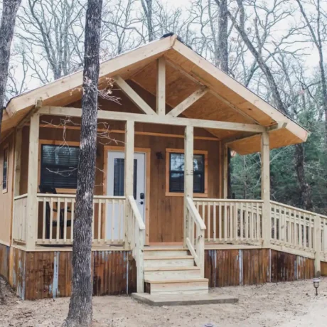 A cozy, wooden cabin nestled in a scenic setting with the sun setting behind it, emphasizing the rustic charm and peaceful atmosphere at Oak Meadow Ranch RV in Valley View, TX.